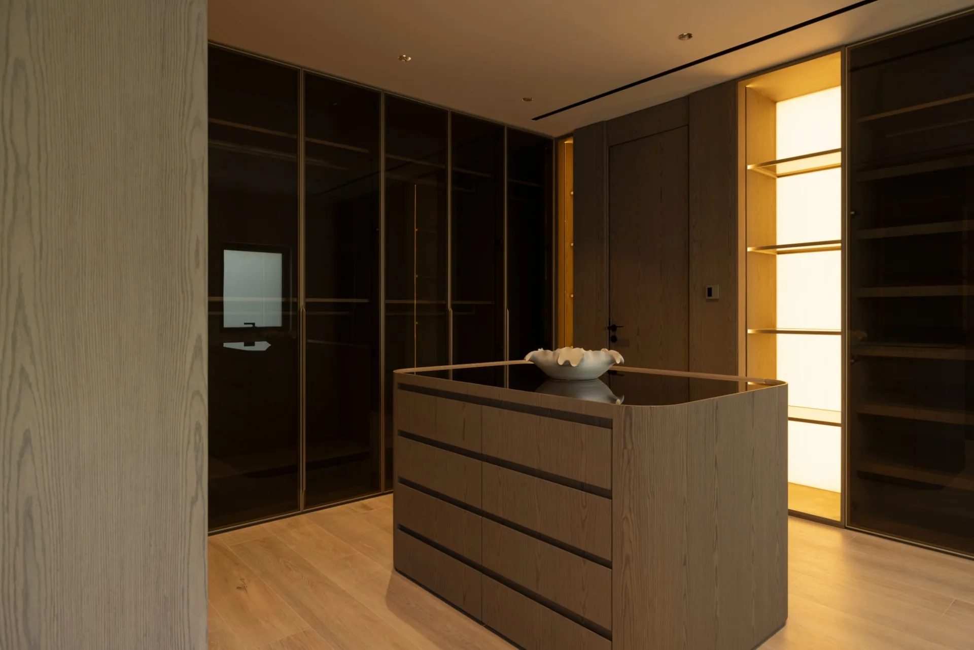 Dressing room with a light oak floor, smoked-glass wardrobes and a wooden island